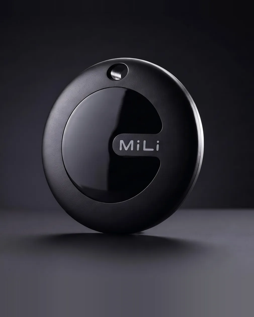 Tracker MiLi MiTag Duo negro, el disco solo con el logo MiLi en la cara frontal, apoyado de canto sobre una superficie oscura