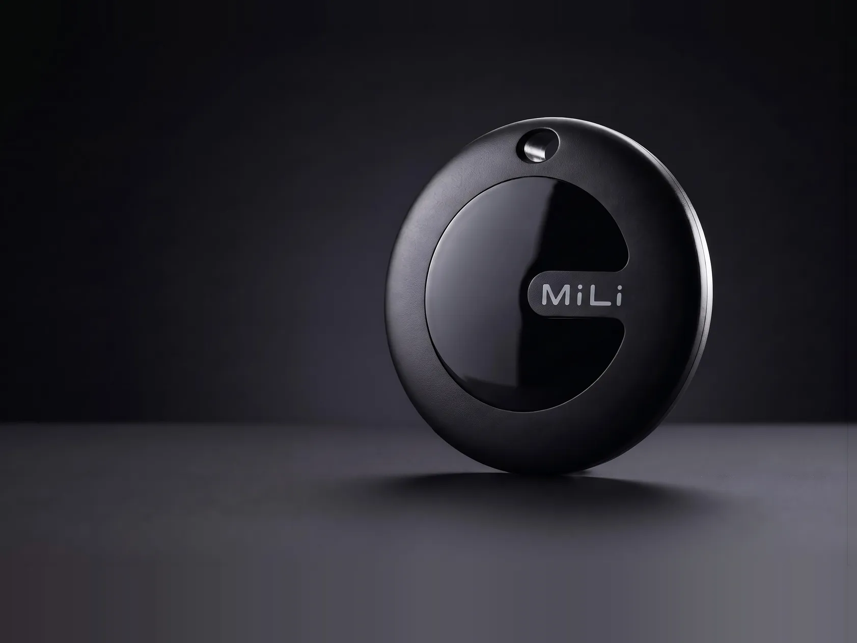 Rastreador MiLi MiTag Duo negro, el disco solo con el logo MiLi en la cara frontal, apoyado de canto sobre una superficie oscura